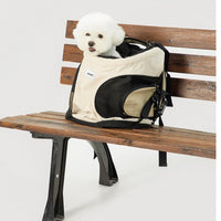 Petit chien blanc transporté dans un sac à dos pour chien respirant en maille posé sur un banc