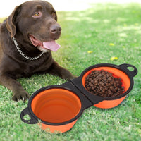 Un chien allongé sur une pelouse devant sa gamelle duo de voyage pliable pour chien de couleur orange rempli d'eau et de nourriture