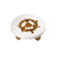 Gamelle pour chien en céramique de couleur blanc avec de la nourriture dedans, en dessus d'un support en bois sur un fond blanc