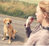 Une femme qui sifflet dans son sifflet ultrason de couleur noir et son chien le regarde