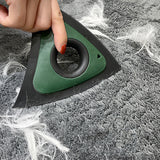 Une main qui tient une brosse à électrostatique de couleur vert et noir et nettoye un tapis de couleur gris plein de poils de chien blanc 