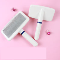 Deux brosses de toilettage blanches pour chien à poil court, avec manche ergonomique et fines aiguilles, posées sur un fond rose avec de petites clochettes.