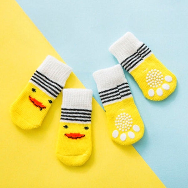 Quatre chaussettes jaunes pour chien avec motifs mignons et semelles antidérapantes blanches, posées sur un fond coloré bleu et jaune.