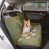Chien assis confortablement sur un couchage vert matelassé installé sur la banquette arrière d’une voiture, avec des sangles fixées aux appuie-têtes pour une sécurité optimale.