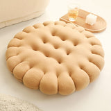 Coussin rond moelleux pour chien, au design biscuit, posé sur un sol clair avec un plateau en bois et une bougie décorative à proximité.