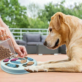 Un chien marron allongé devant sa gamelle anti-glouton rond bleue se faisant remplir de friandises