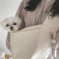 Un petit chien blanc dans un sac en forme de bandoulière de couleur blanc porté par une femme