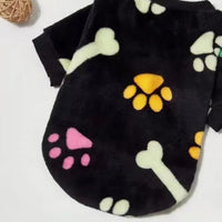 pull pour chien en polaire noire posé à plat avec des os et des pattes jaunes roses et verts
